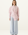 Esmaee Bayview button-up shirt in pink stripe with a wrap-front waist detail and long sleeves, worn with light blue trousers.