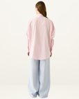 Back view of the Esmaee Bayview pink striped button-down shirt with long sleeves paired with light blue wide-leg trousers.