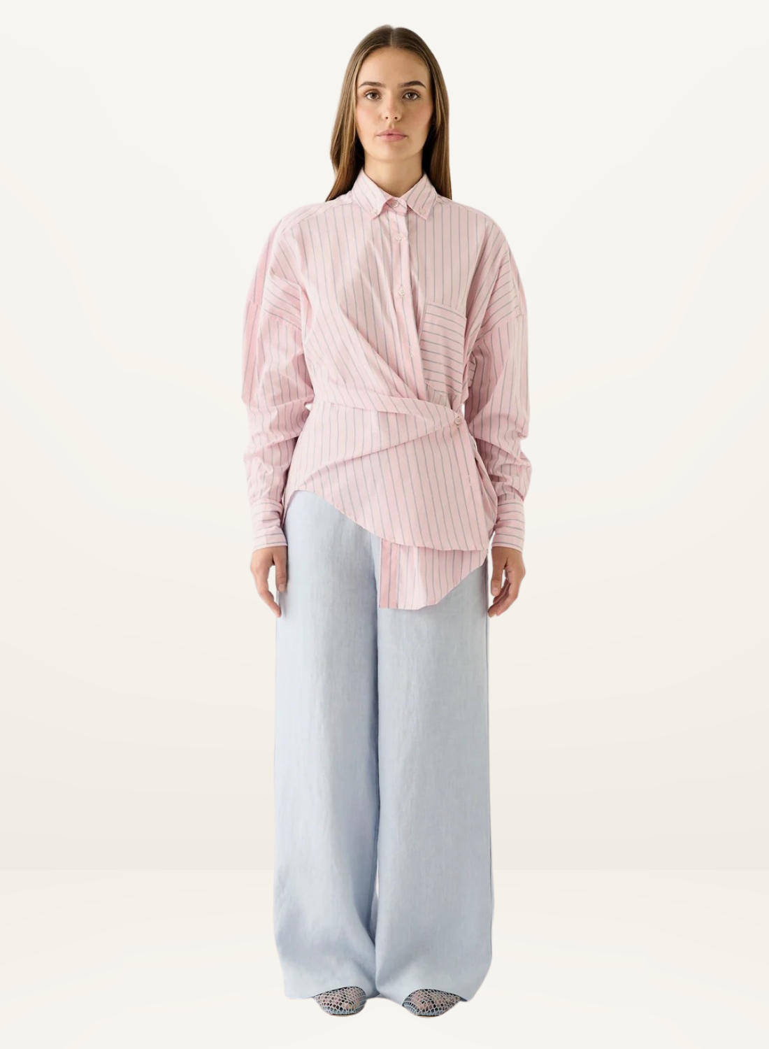 Esmaee Bayview button-up shirt in pink stripe with a wrap-front waist detail and long sleeves, worn with light blue trousers.