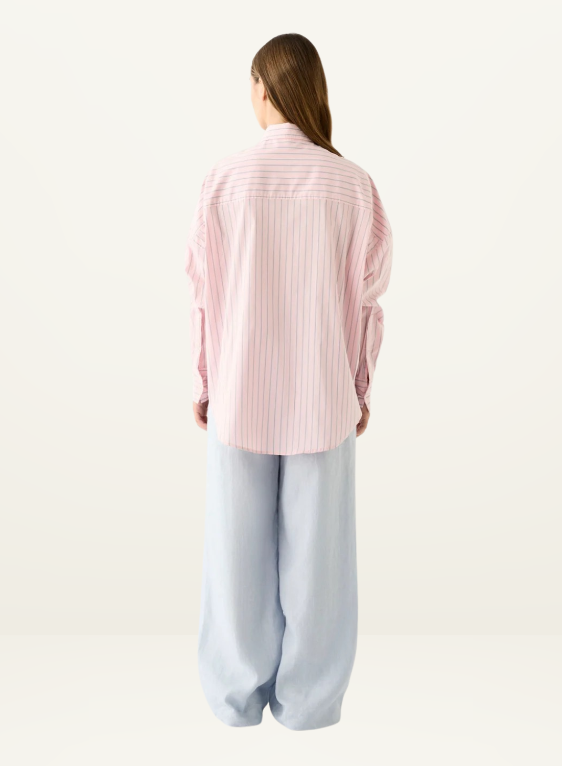 Back view of the Esmaee Bayview pink striped button-down shirt with long sleeves paired with light blue wide-leg trousers.