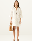 Model wearing a white mini shirt dress in eyelet embroidery fabric with a button-down collar and elbow-length sleeves.