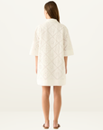Back view of a white Esmaee mini dress featuring intricate eyelet embroidery, a collared neckline, and elbow-length sleeves.