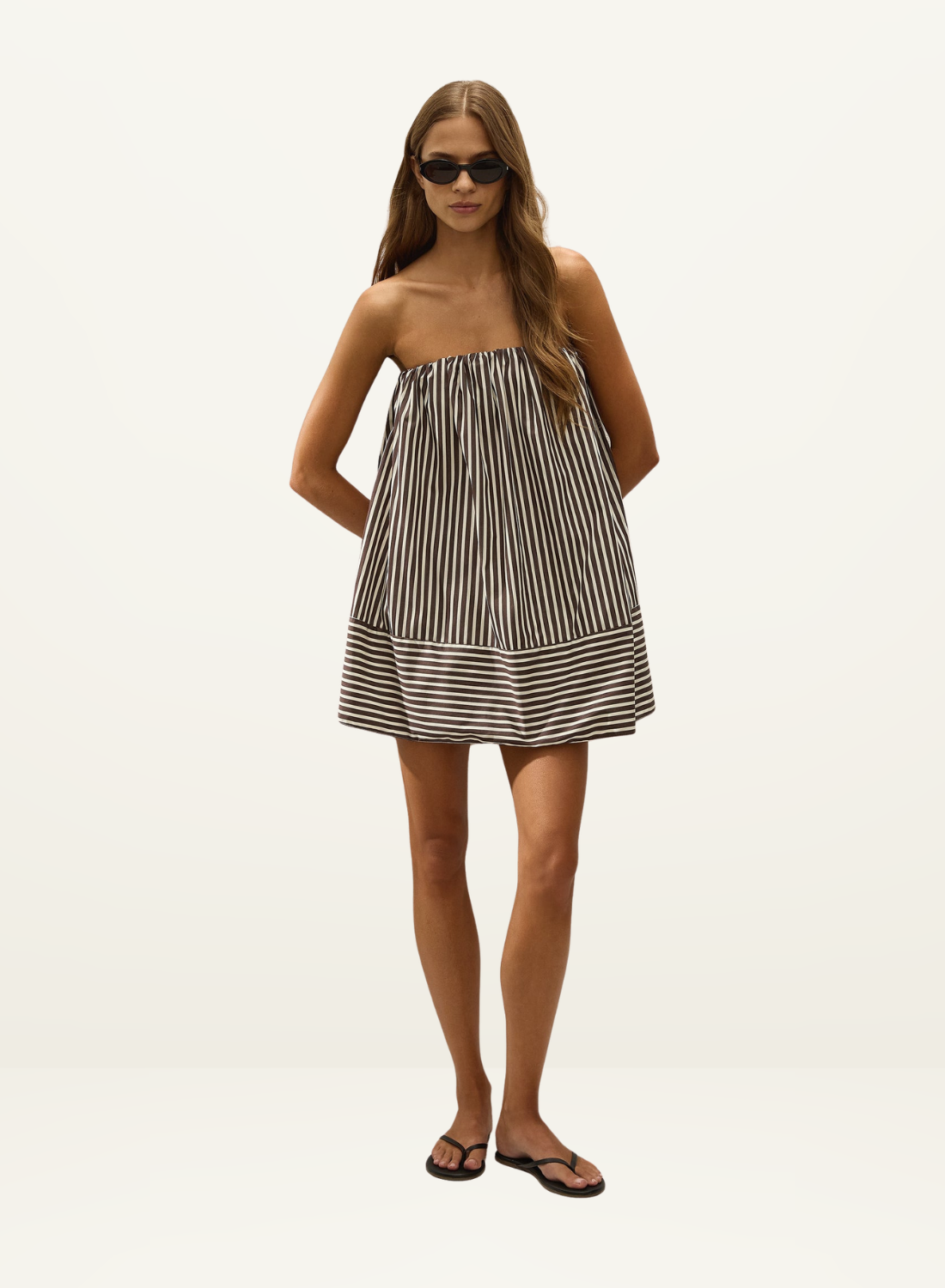 Model wearing a strapless Faithfull Camila mini dress in Rita stripe port cotton with a relaxed tent silhouette.