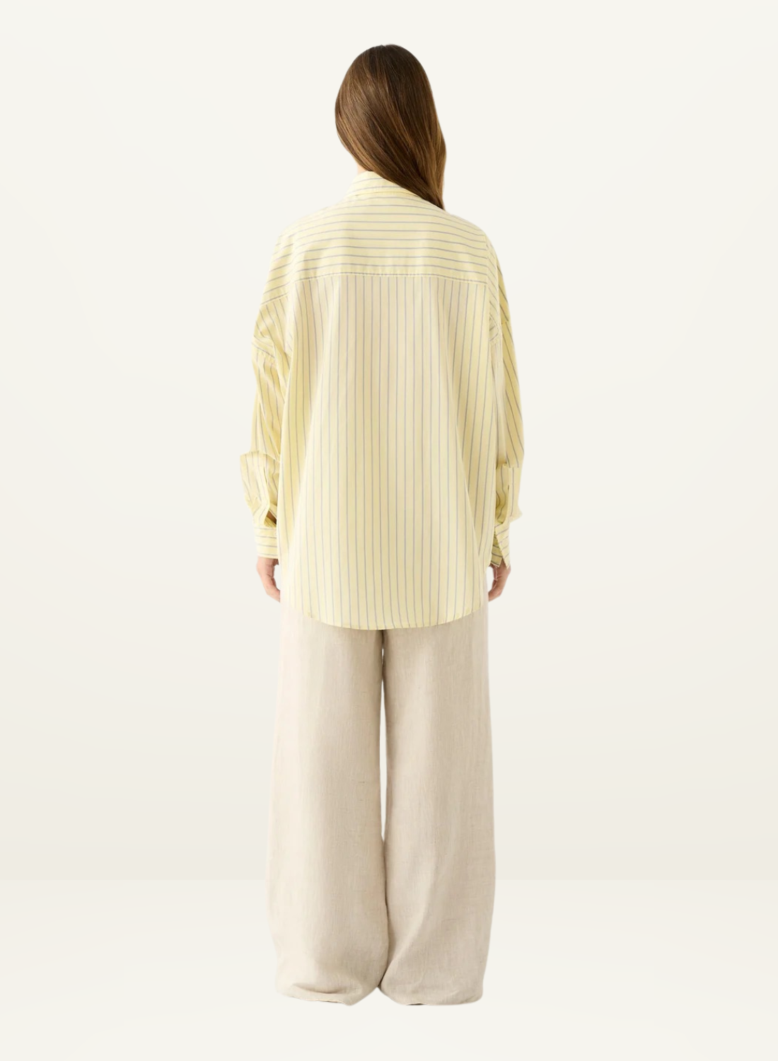 Back view of Esmaee Bayview oversized shirt in lemon yellow and white vertical stripes, paired with beige wide-leg trousers.