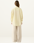 Back view of Esmaee Bayview oversized shirt in lemon yellow and white vertical stripes, paired with beige wide-leg trousers.