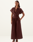 Model wearing a chocolate brown Sovere Lyra midi dress in stretch cotton with a pleated waistband and magyar sleeves.