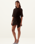Model wearing a black cotton mini tee dress with a cinched waist, pleated side detail, and asymmetric hem.